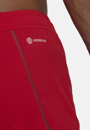 Shorts de sport rouges avec une texture lisse, des coutures grises contrastantes et le logo "AEROREADY" sur le côté.