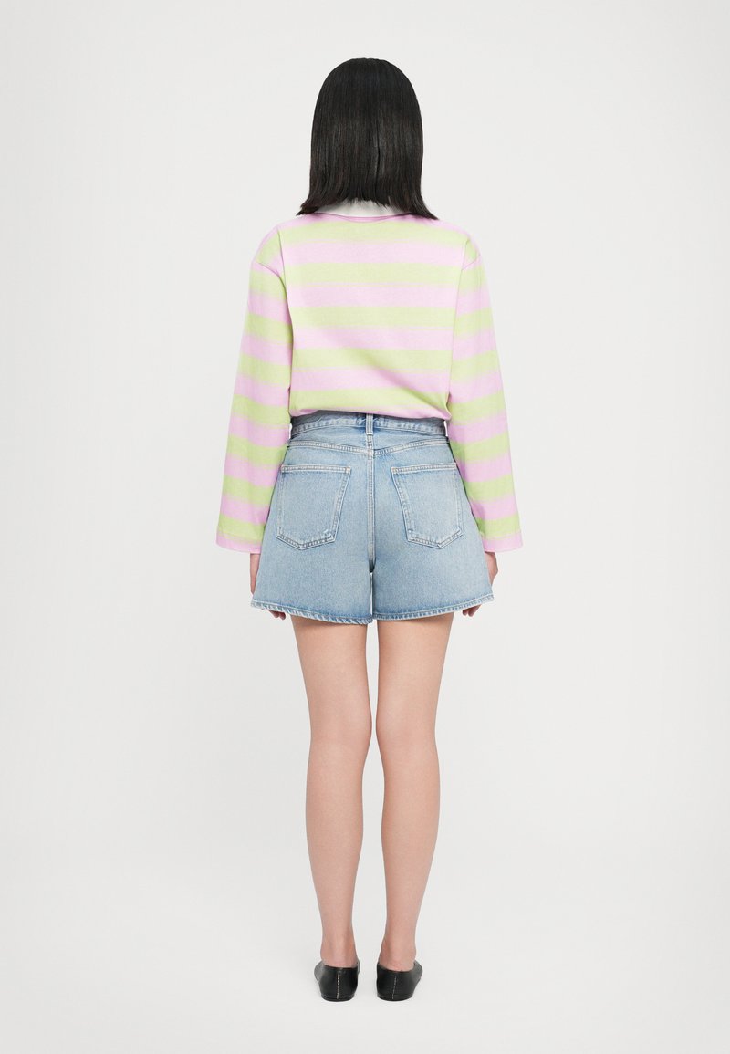 Sweatshirt léger avec des rayures horizontales roses et vertes, associé à un short en denim taille haute. Des chaussures noires à enfiler complètent le look.