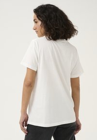T-shirt en coton blanc à manches courtes, col rond et coupe décontractée. Texture lisse, sans motifs ni graphiques visibles.