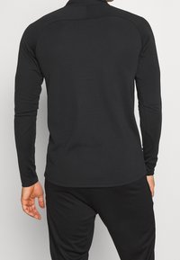 Long-sleeve, fitted black athletic top made of smooth fabric, featuring a high collar and seamless shoulders for comfort and flexibility.