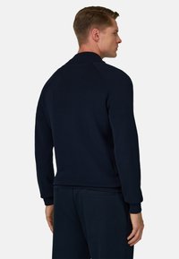 Sudadera azul marino de cuello redondo con textura suave, puños y dobladillo acanalados. Presenta un diseño simple sin logotipos ni patrones visibles.