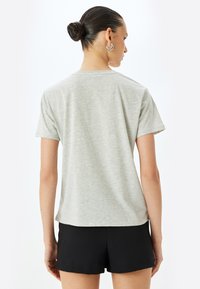 Grå kortærmet t-shirt lavet af blødt stof, med en afslappet pasform og en rund kant. Båret med sorte shorts, der fremhæver et minimalistisk design.