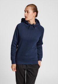 Granatowa bluza z kapturem ze sznurkiem, z raglanowymi rękawami i miękką fakturą. Posiada ściągacz u dołu i na mankietach, zestawiona z czarnymi spodniami.