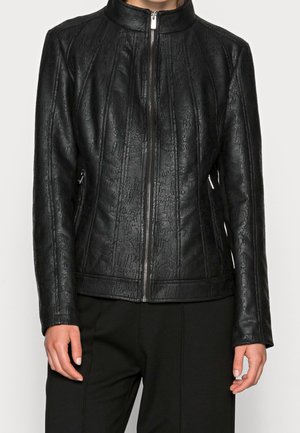 Vrouw draagt een nauwsluitend zwart textuur zip-up jack met opstaande kraag en verticale naaddetails, gecombineerd met een zwarte broek.