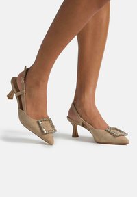 Scarpe slingback in suede beige con punta appuntita, dotate di una fibbia quadrata decorativa arricchita da cristalli e di un tacco a blocco corto.