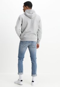 Sudadera con capucha gris de ajuste entallado, combinada con jeans azul claro y zapatillas blancas, con puños doblados y dobladillo acanalado.