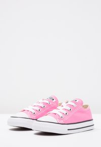 Rosa lerret-sneakers med hvit gummiskap, svart stripe på sålen og hvite snørebånd; glatt tekstur med kontrasterende sømdetaljer.