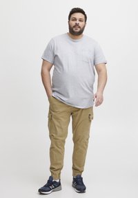 Grå bomullströja med ficka, i kombination med beige cargobyxor med sidfickor och elastiska muddar. Modellen bär marinblå sneakers.