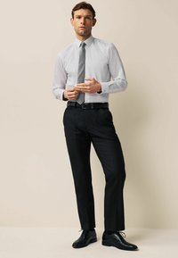 Jasnoszara koszula, czarne spodnie slim-fit i czarne sznurowane buty. Koszula ma klasyczny kołnierzyk i mankiety na guziki, oraz teksturowany krawat.
