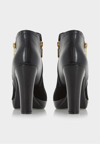 Zapatos de tacón alto negros con un acabado de cuero suave y un panel de ante. Acentos de herrajes dorados y un diseño de punta redondeada.