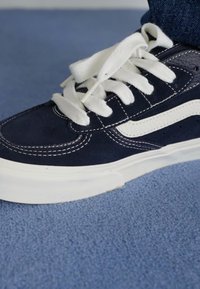 Morn navy plavi velur patike s bijelim vezicama, bijelim bočnim prugama i teksturiranom potplatom. Vidljive šavove na gornjem delu i bočnom dijelu.