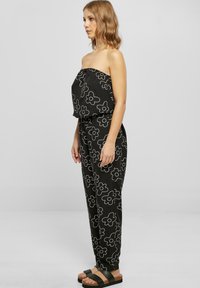 Czarny, bezramienny kombinezon z białym kwiatowym wzorem, w luźnym fasonie, ze zwężającymi się nogawkami, długość do kostek. Połączony z czarnymi sandałami na płaskiej podeszwie.