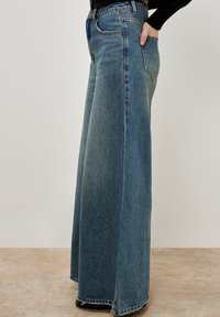 Wijduitlopende blauwe denim jeans met een hoge taille, contrasterende stiksels en een ontspannen pasvorm. Het materiaal is zacht met een vervaagd uiterlijk.