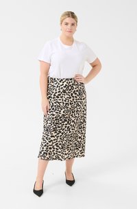 Jupe midi en tissu léger à imprimé léopard, avec un motif noir et beige, associée à un t-shirt blanc à manches courtes et des escarpins noirs pointus.