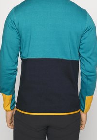 Maglione color block con parte superiore turchese, parte centrale blu navy e polsini gialli. Realizzato in materiale morbido, presenta cuciture a vista lungo le cuciture.