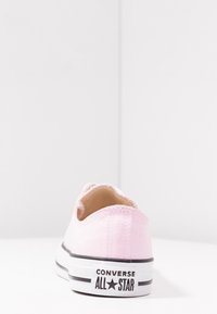 Tylny widok jasnoróżowego niskiego trampka Converse All Star na białej powierzchni na tle jednolitego białego tła.
