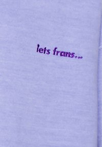 Tessuto lilla con ricamo in viola scuro che recita "lets frams..." con una consistenza morbida e liscia.