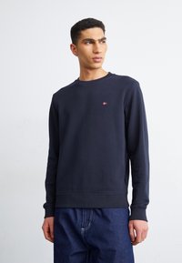 Felpa blu navy con maniche lunghe, collo e polsini a coste, caratterizzata da un piccolo emblema rosso sul petto. Tessuto morbido.