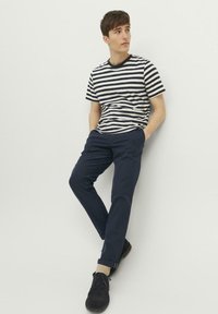 Gestreiftes T-Shirt in Marineblau und Weiß, kombiniert mit Marineblauen Chinos. Das Outfit hat einen lockeren Schnitt, ein glattes Material und schwarze Schuhe.