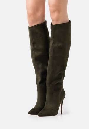 Grüne Wildleder-Stiefel über dem Knie mit einer spitzen Zehe und Stiletto-Absatz, die über eine glatte Textur und minimale Nähte verfügen.