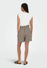 Pantaloni corti grigi con un elastico in vita e una tasca sul retro, abbinati a un top bianco senza maniche. Modello visto da dietro.