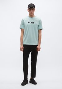 Heleroheline puuvillane T-särk musta "BOSS" trükiga, mida täiendab mustad kitsenevad püksid ja mustad tossud, millele lisandub must nokamüts.