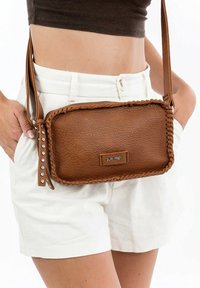 Borsa a tracolla in pelle marrone con bordi intrecciati e dettagli in metallo argentato. Forma rettangolare, superficie testurizzata, tracolla regolabile.