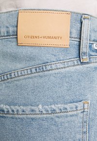 Vaaleansiniset farkut, joissa on takataskussa yläpuolella ommeltu vaaleanruskea nahkainen merkkilappu, jossa lukee "CITIZENS of HUMANITY".