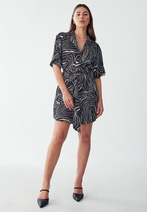 Black dress with white abstract line patterns, short sleeves, a belted waist, and a wrap design. Worn with black pointed shoes.