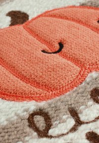 Décoration en tissu de citrouille orange avec des détails texturés ; placée sur un fond brun clair avec des lettres et des accents brodés en marron foncé.