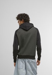 Sweatshirt à capuche avec un corps gris foncé et des manches noires. Il présente des poignets et un ourlet côtelés, une texture douce et une coupe décontractée.