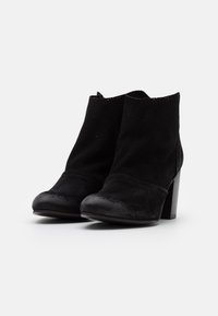 Botas ankle negras de ante con acabado mate, que presentan una puntera redondeada y un tacón cuadrado de altura media, diseñadas con detalles perforados.