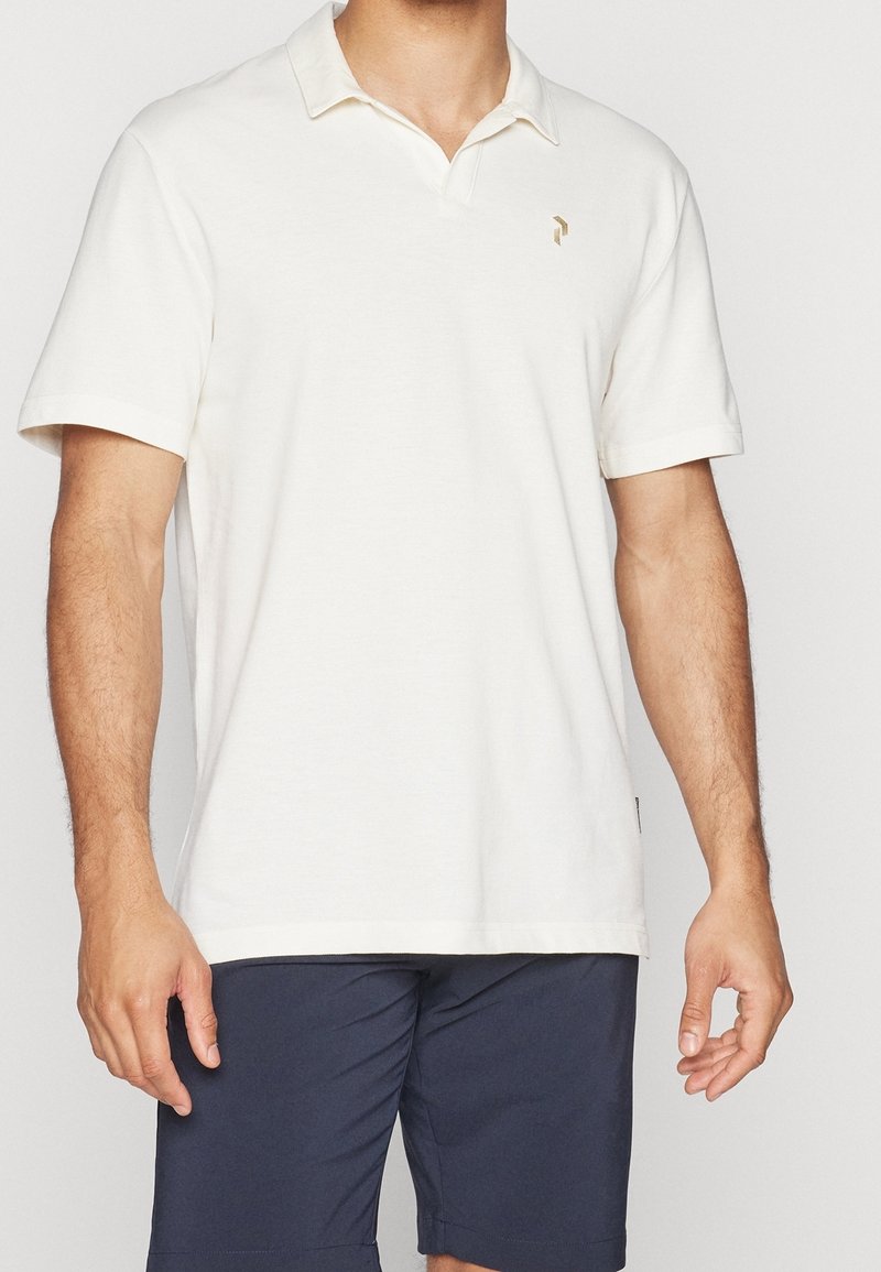 Kortærmet polo-shirt i creme med en foldet krave, der har et lille guld logo på brystet, lavet af blødt bomuldsstof.