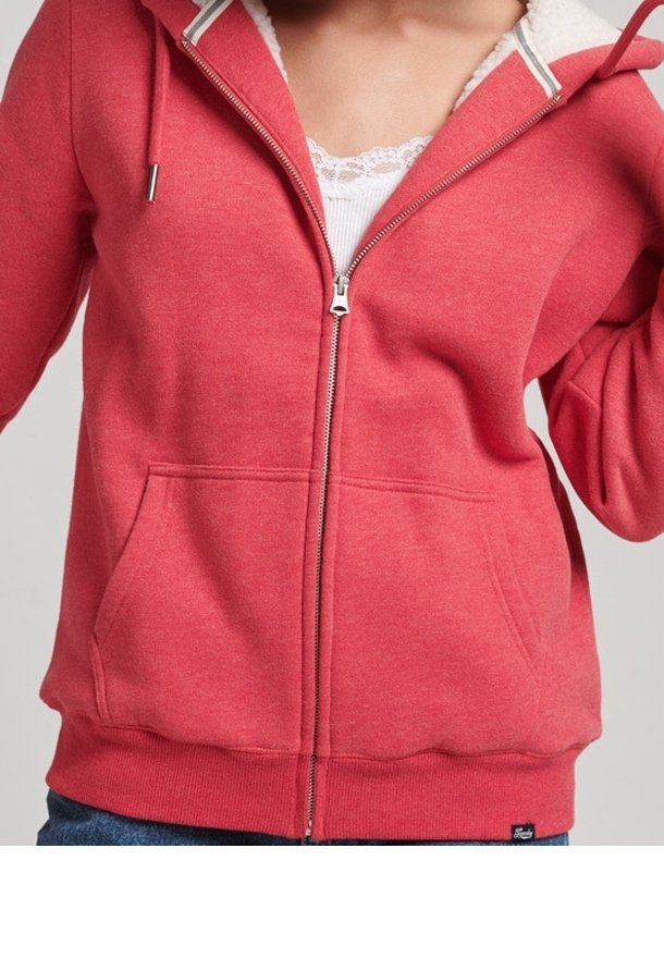 Person wearing a red zip-up hoodie over a white lace-trimmed top, with hands partially raised and the zipper closed.