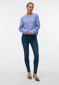 Světle levandulový pletený svetr s dlouhými, mírně nabíranými rukávy, kombinovaný s tmavě modrými skinny džíny a černými sandály na podpatku.