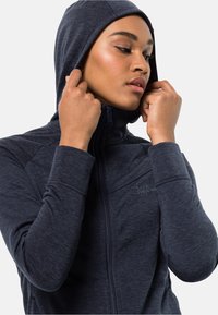 Felpa con zip di colore blu navy, con una texture morbida, design aderente e colletto alto. Presenta il logo sul petto e un cappuccio avvolgente.