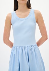 Robe sans manches bleu clair avec un haut côtelé et une jupe froncée. Présente un col rond et une texture douce et fluide dans le bas du tissu.