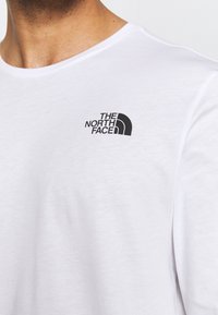Vit kortärmad t-shirt med rund krage. Har en svart logotyp av "The North Face" i vänster bröstområde. Mjuk tygtextur.