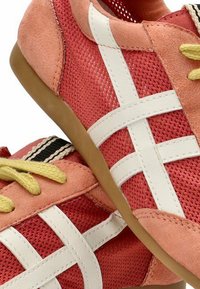 Zapatillas deportivas rojas y rosas con parte superior de malla, detalles en blanco, cordones amarillos y una suela de goma con detalles en negro en la lengüeta.