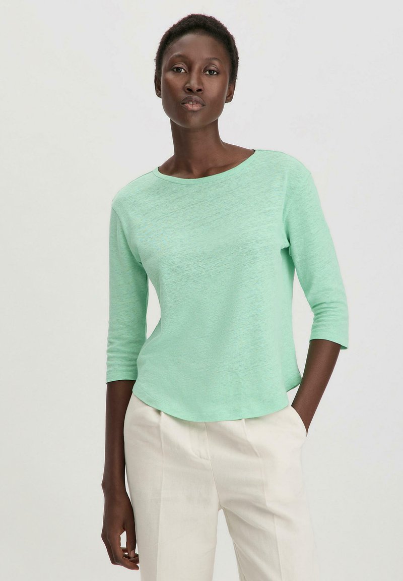 Haut léger à manches longues vert menthe avec un col rond et un ourlet légèrement arrondi. Porté avec un pantalon crème.