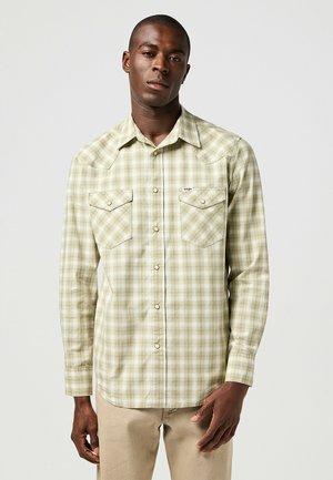 Camisa de cuadros verdes de manga larga con dos bolsillos frontales, cierre de botones y cuello puntiagudo. Fabricada con una tela liviana y de textura suave.