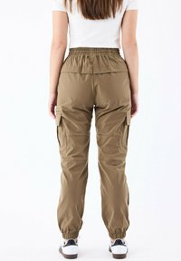 Pantalones cargo color caqui con cintura elástica, bolsillos laterales y tobillos ajustados. El material parece suave, diseñado para la comodidad y la utilidad.