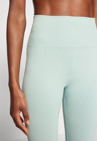 Leggings ribbed verde menta con un alto punto vita, realizzati in un tessuto testurizzato e stretch. Ingrandimento del dettaglio del tessuto e posizione della mano.