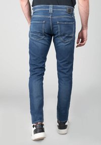 Jeans de mezclilla azul ajustados que cuentan con bolsillos traseros, un parche de cuero de la marca y un ligero desgastado. Combinados con zapatillas negras y blancas.