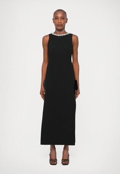 Robe noire sans manches avec un encolure arrondie ornée de cristaux. Coupe droite jusqu'au sol, design minimaliste, texture élégante.