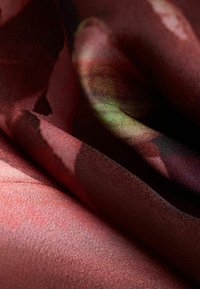 Material cu model floral în nuanțe de roșu și verde, caracterizat printr-o textură netedă și o cădere moale, cu straturi suprapuse care creează profunzime.