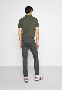 Polo-shirt vert foncé, pantalon slim gris et chaussures blanches avec des accents rouges. La vue montre l'arrière, affichant un design simple et une texture de tissu.