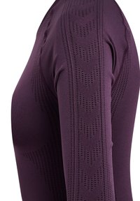 Lila sportströja med lång ärm som har texturerade mönster och perforerade detaljer längs ärmarna. Tyget ser slätt och elastiskt ut.