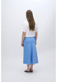 Hvid cropped t-shirt parret med en lang, svævende blå nederdel. Nederdelen har en glat tekstur og en let glans, med simple sandaler.