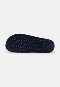 Shoe sole in dark navy rubber with a zigzag tread pattern. Features a smooth texture and circular accents in the design.
